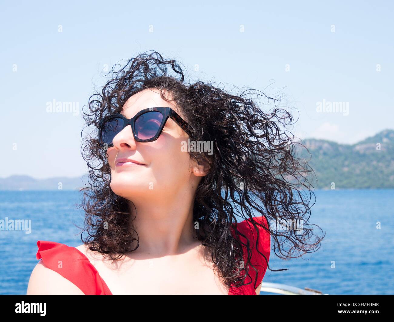 Portrait de belle femme de cheveux bouclés à l'extérieur sur la plage bleue eau de mer, visage souriant heureux, concept d'été Banque D'Images