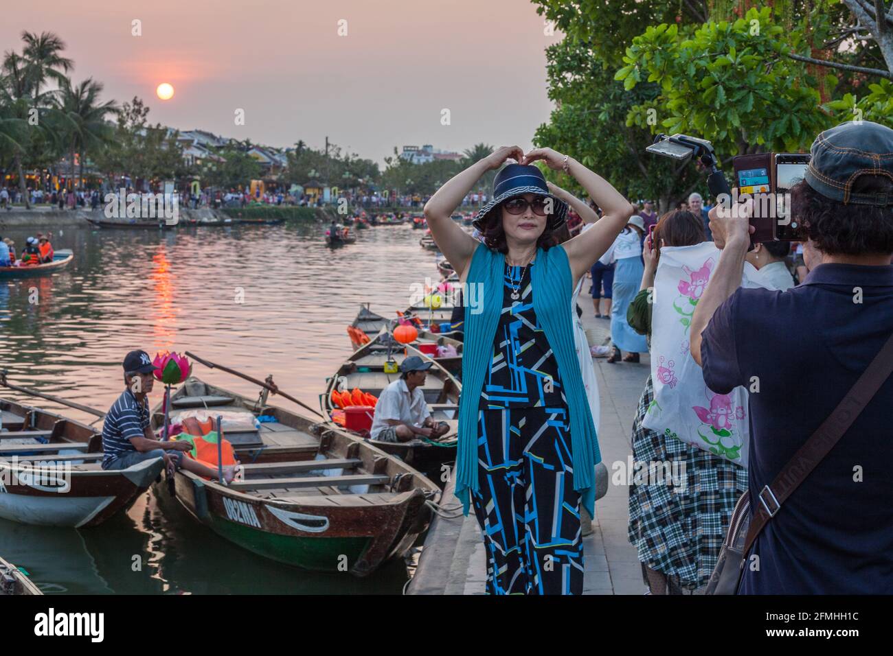 Tourist pose avec les mains au-dessus de sa tête avec le soleil se coucher derrière elle comme partenaire prend la photo, Hoi an, Vietnam Banque D'Images