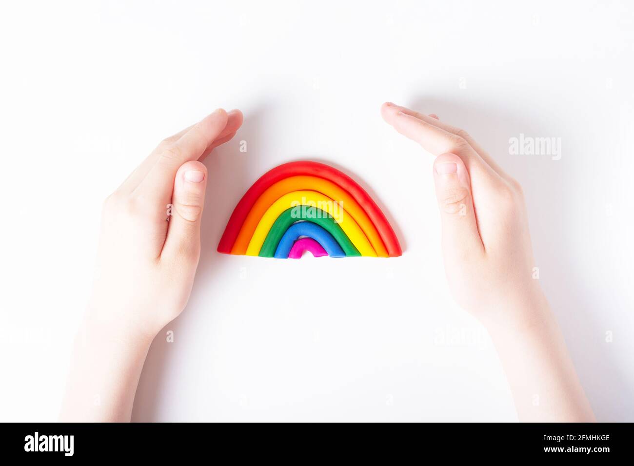 Les mains des enfants autour de la plasticine arc-en-ciel. Concept de famille LGBT. Vue de dessus. Couleurs du drapeau gay. Arrière-plan clair. Banque D'Images