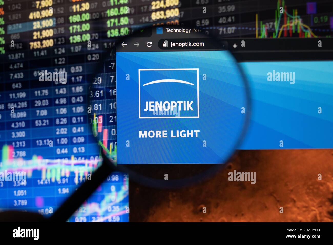 Logo de la société Jenoptik sur un site web avec des développements flous de marché boursier en arrière-plan, vu sur un écran d'ordinateur à travers une loupe Banque D'Images