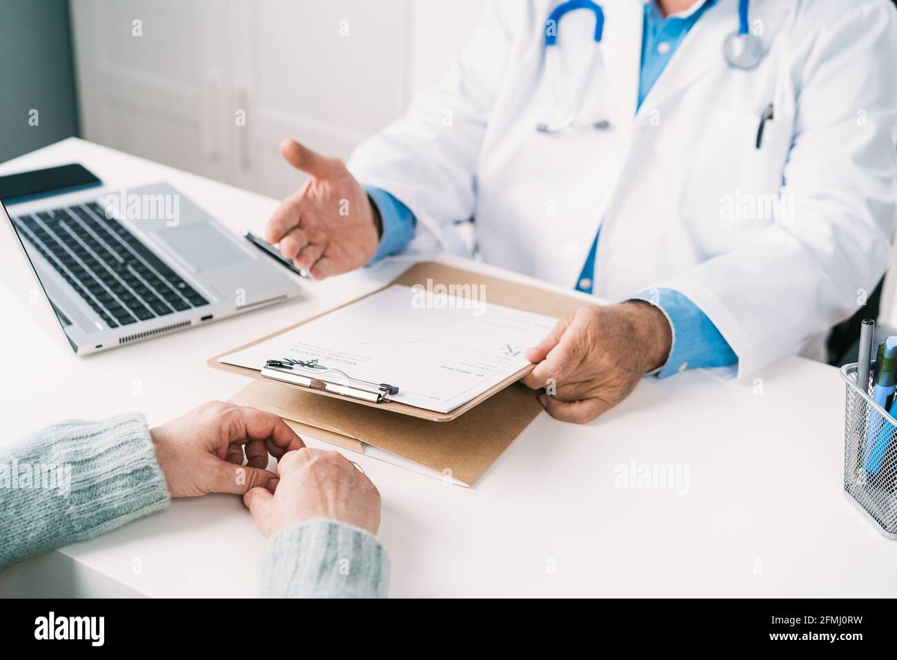 Un médecin masculin âgé non reconnaissable a été mis en culture sous forme uniforme sur la planchette à pince de la table contre une femme méconnaissable pendant le contrôle clinique Banque D'Images