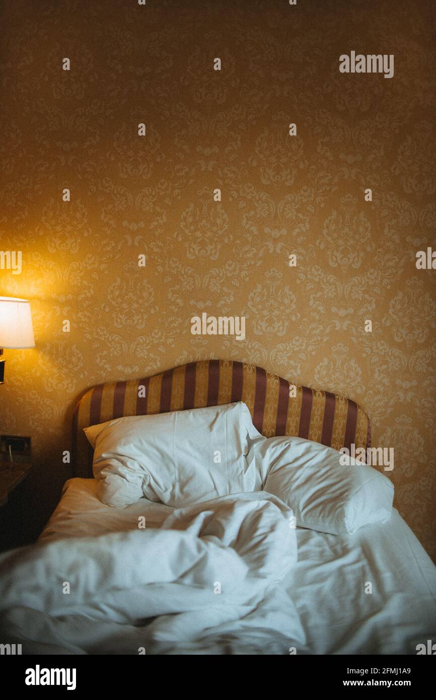 Intérieur de la chambre avec draps froissés et couverture sur le lit contre le mur décoratif et la lampe Banque D'Images