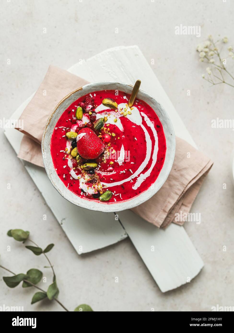 Vue de dessus d'un bol de soupe aux baies fraîches et sucrées avec pistaches servies sur la planche à découper sur la table Banque D'Images