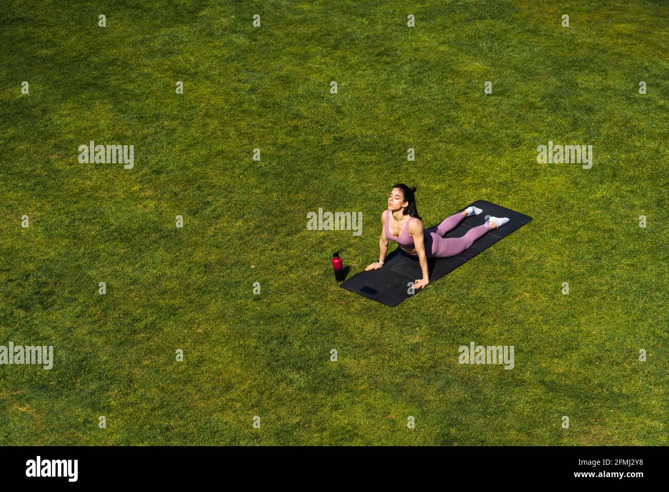 De dessus de jeune femme dans les vêtements de sport exécutant Urdhva Mukha Svanasana pose tout en pratiquant le yoga sur la pelouse Banque D'Images