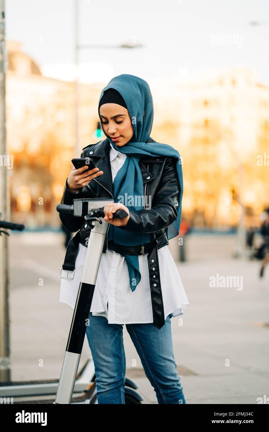 Contenu Femme musulmane dans un foulard traditionnel à l'aide de  l'application sur smartphone et affichage de lecture pour déverrouiller le  scooter électrique moderne stationné sur ville rade Photo Stock - Alamy