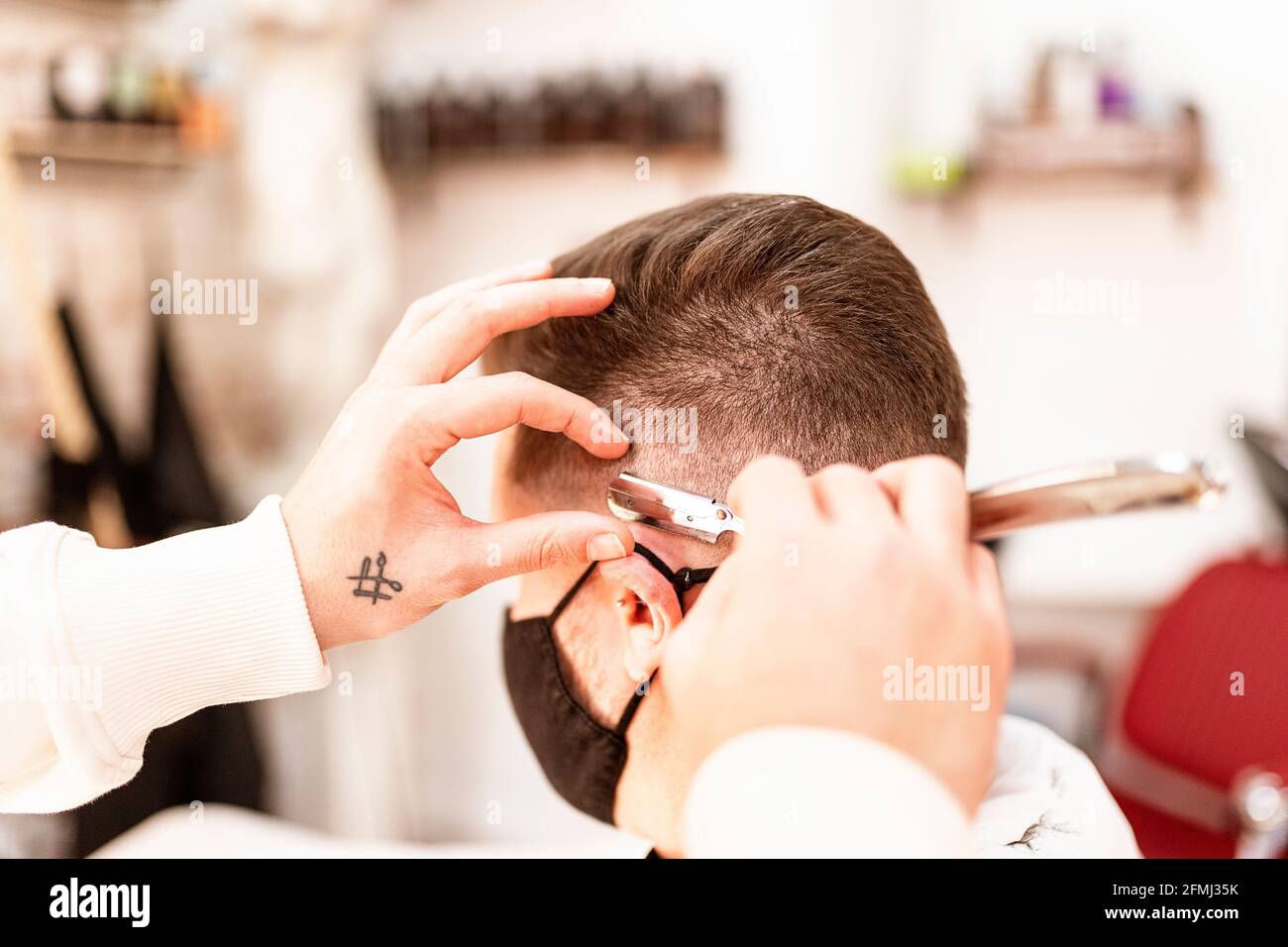 Crop anonyme coiffeur rasoir homme en masque avec rasoir droit en barbershop sur fond flou Banque D'Images