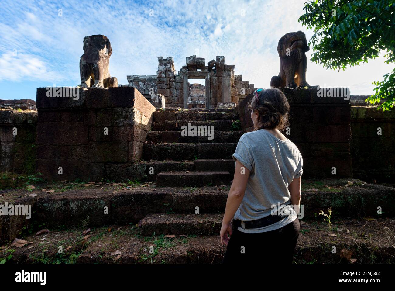 Vue arrière d'une touriste féminine anonyme contemplant un animal en pierre vieilli Statues et escaliers à Angkor Wat du Cambodge Banque D'Images