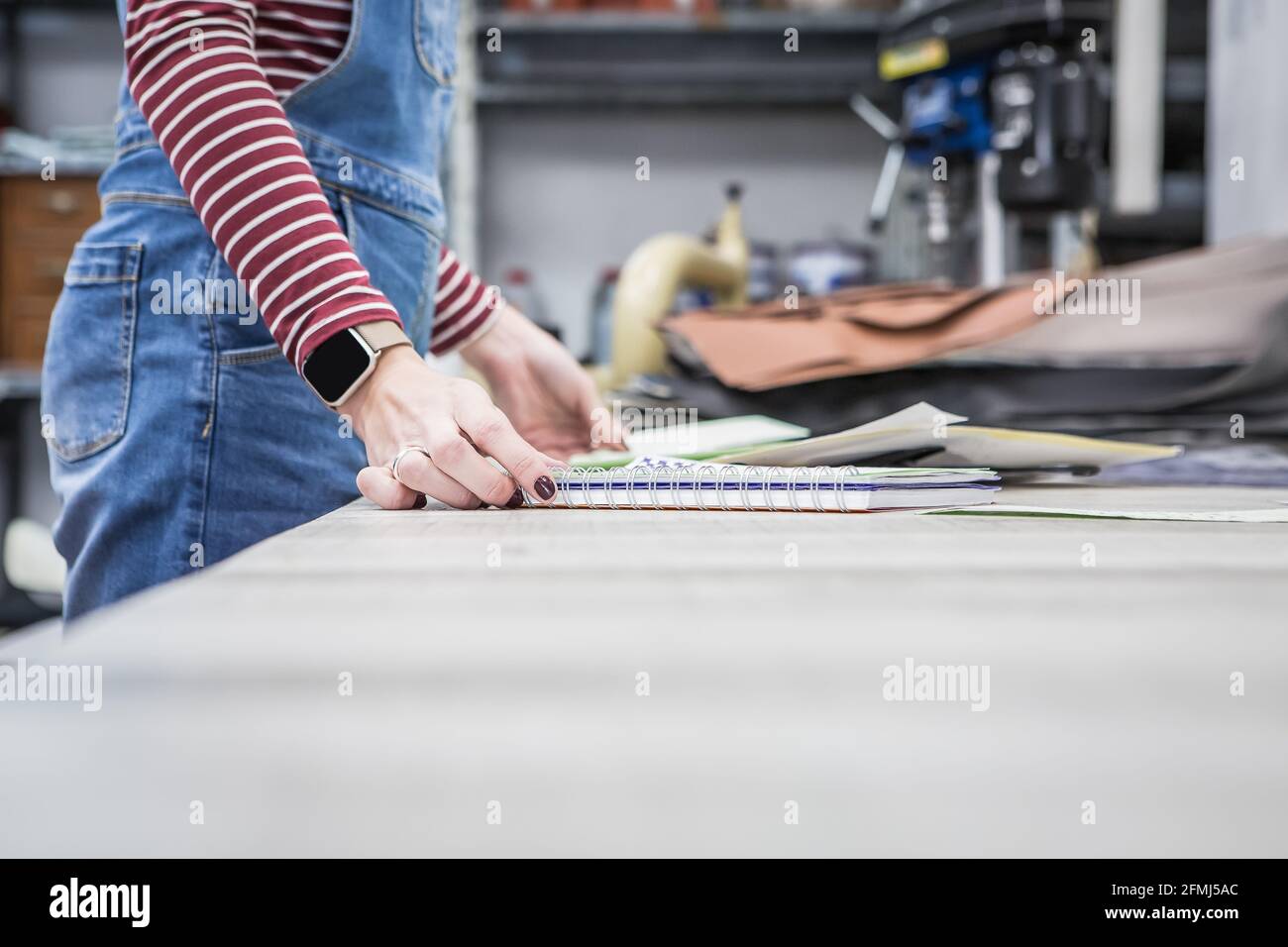 Vue latérale à angle bas de la récolte anonyme femme artisan debout avec blocs-notes et tissus assortis à l'établi dans la garniture de moto atelier Banque D'Images