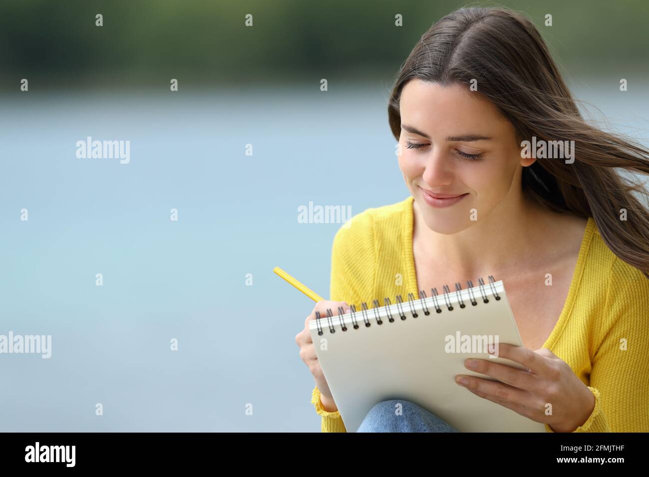 Bonne femme à dessiner dans un carnet assis près d'un lac Banque D'Images