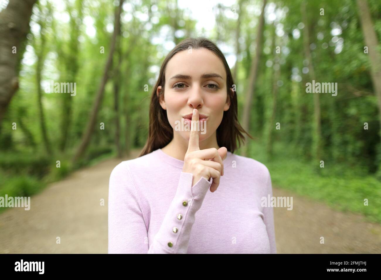 Vue de face d'une belle femme demandant le silence dans une forêt Banque D'Images