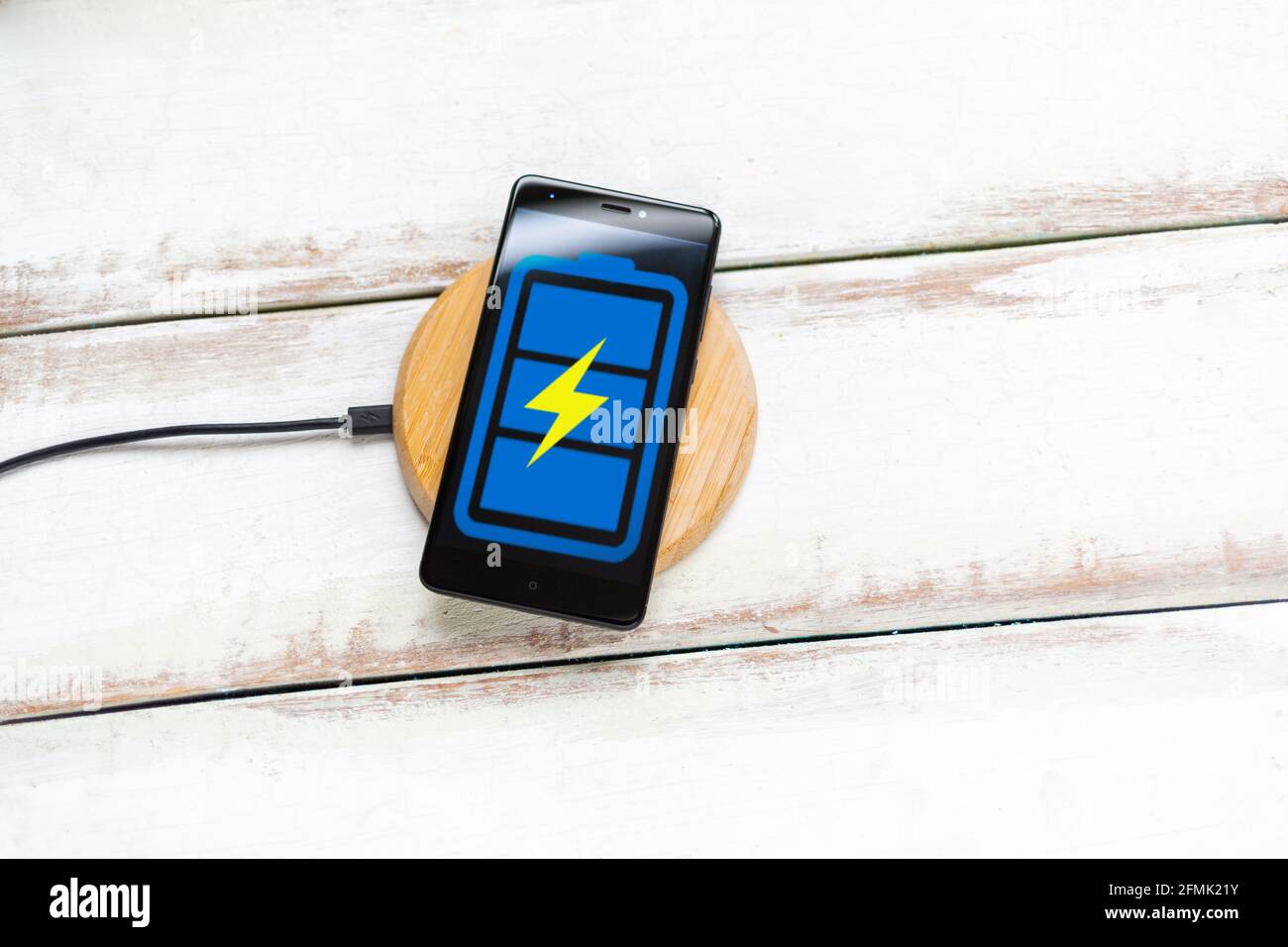Concept des technologies modernes. Sur le chargeur sans fil se trouve un smartphone noir avec une icône de batterie bleue. Arrière-plan en bois blanc avec bande horizontale Banque D'Images