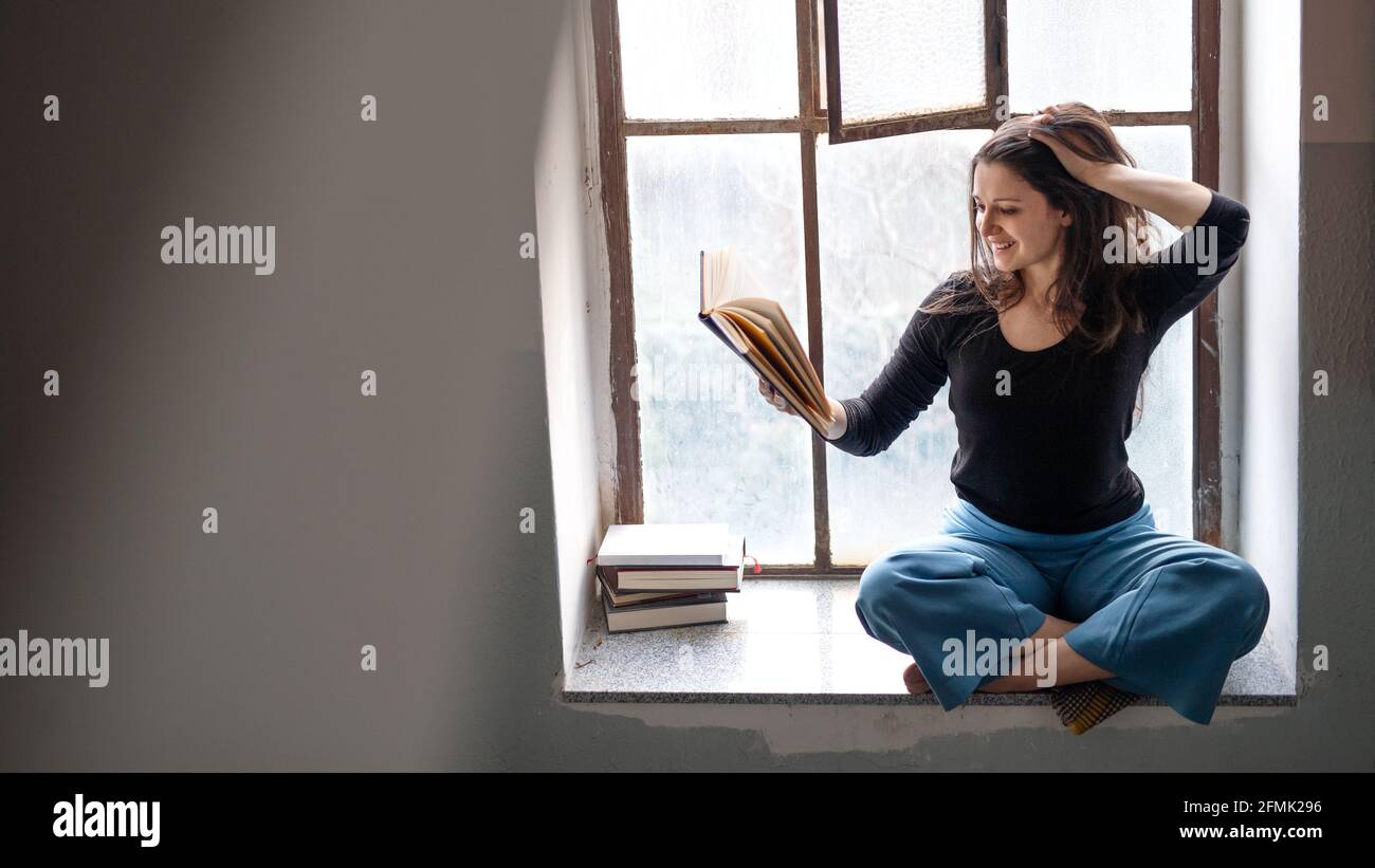 Une femme heureuse assise sur un vieux et sale rebord de fenêtre, lisant un livre. Banque D'Images