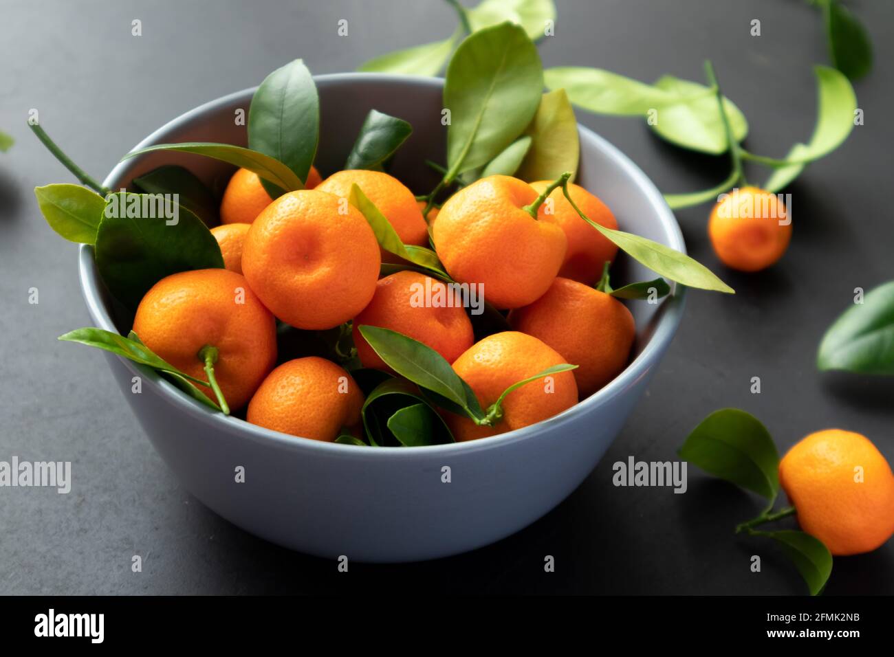 Mandarines fraîchement cueillies avec feuilles sur plaque sur fond noir. Banque D'Images