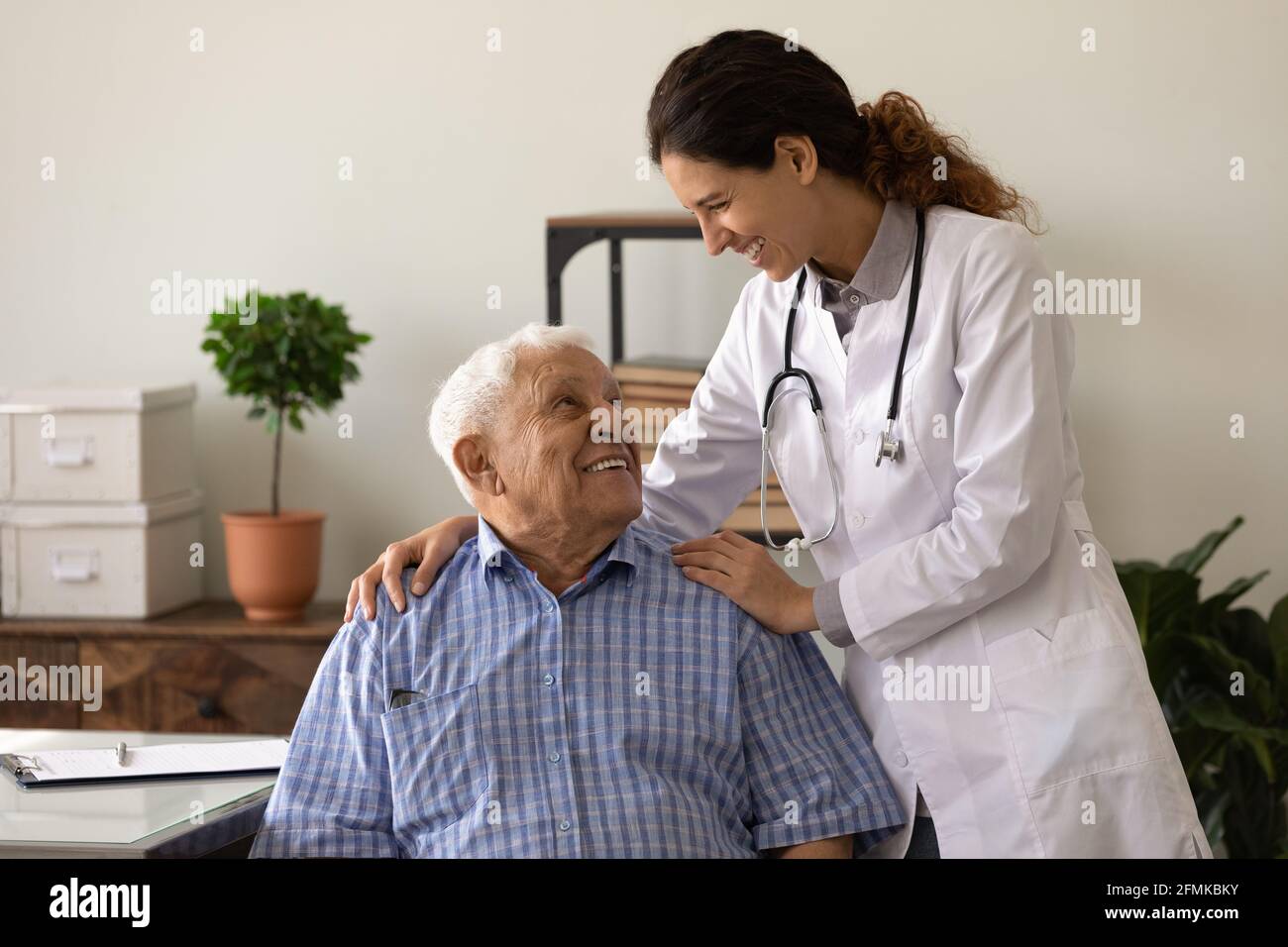 Optimiste femme doc embrasser les épaules de rire vieux homme patient Banque D'Images
