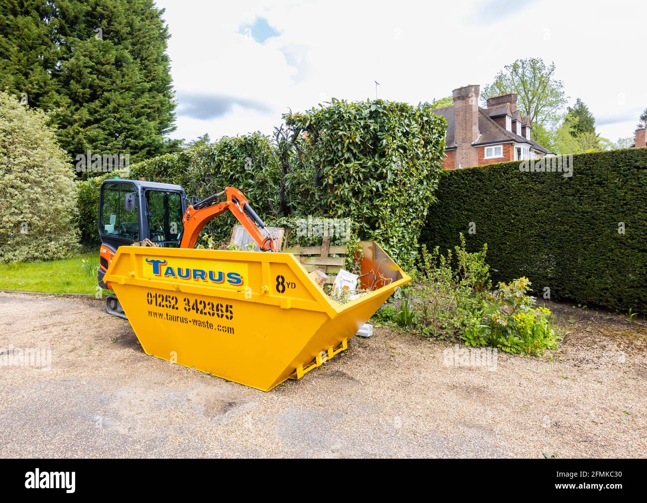 Un véhicule à chenilles en caoutchouc, une minipelle Kubota KX016-4 orange et un saut jaune utilisé pour le dégagement du jardin et l'enlèvement des débris, Surrey, Angleterre Banque D'Images