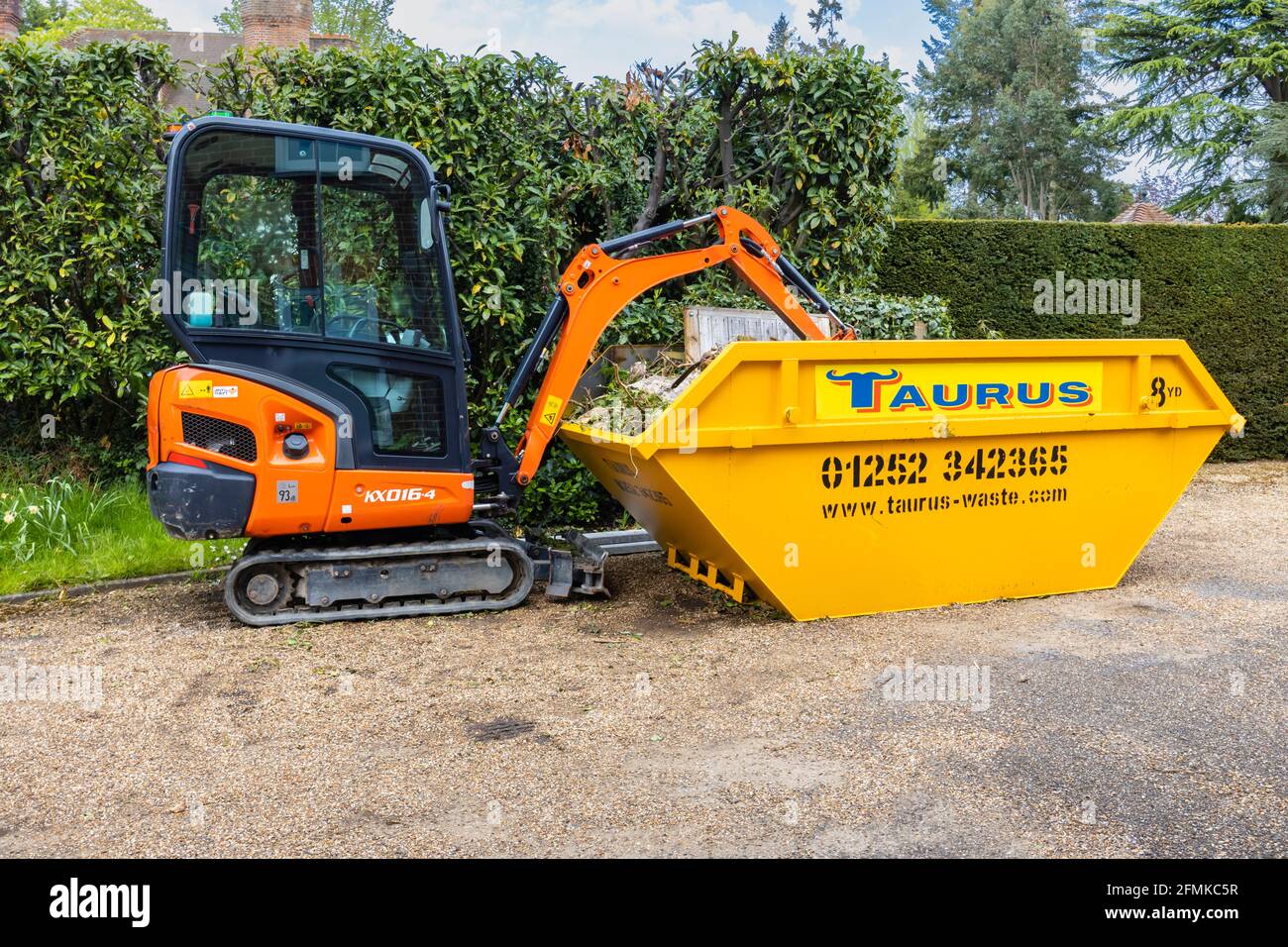 Un véhicule à chenilles en caoutchouc, une minipelle Kubota KX016-4 orange et un saut jaune utilisé pour le dégagement du jardin et l'enlèvement des débris, Surrey, Angleterre Banque D'Images