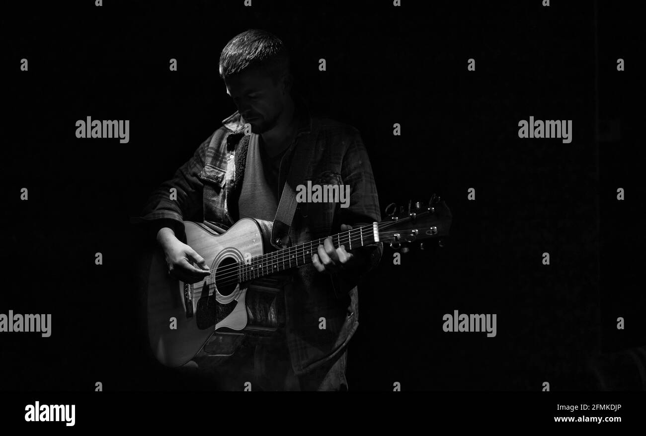 Guitariste masculin jouant de la guitare acoustique dans une pièce sombre. Banque D'Images