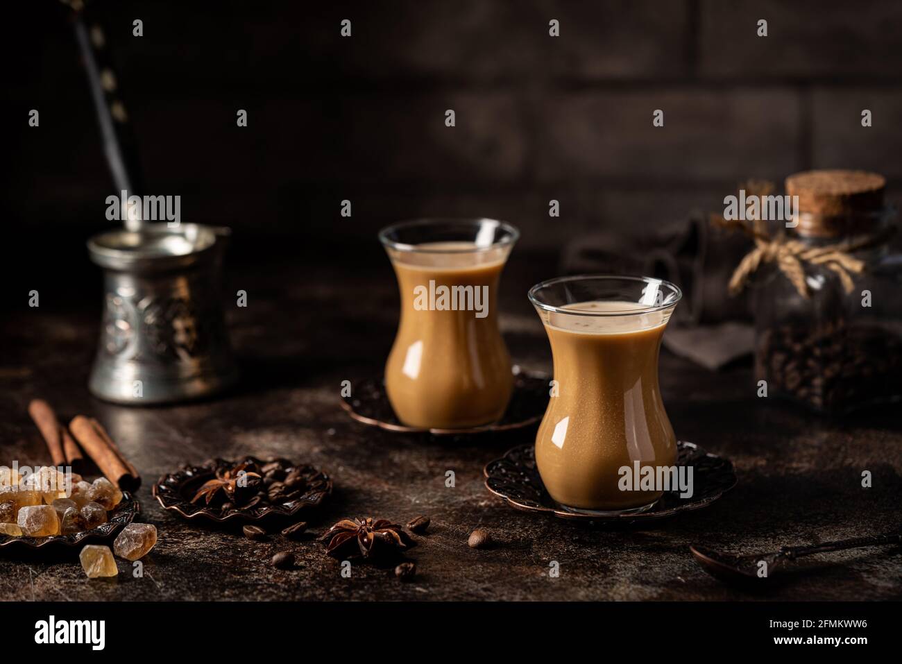 Thé ou café avec lait et épices en verre Armudu avec grains de café et sucre sur fond sombre. Banque D'Images