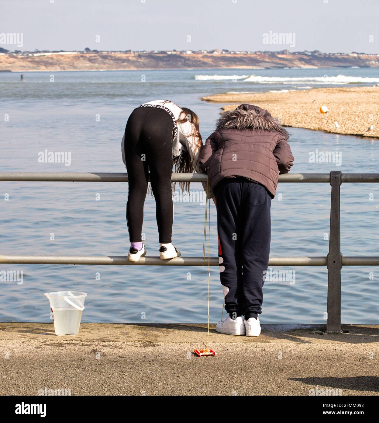 Vue arrière de deux jeunes filles, enfants avec UN seau de pêche aux crabes penchée sur des rampes qui regardent l'océan attraper des crabes, crabes à Mudeford Quay Banque D'Images