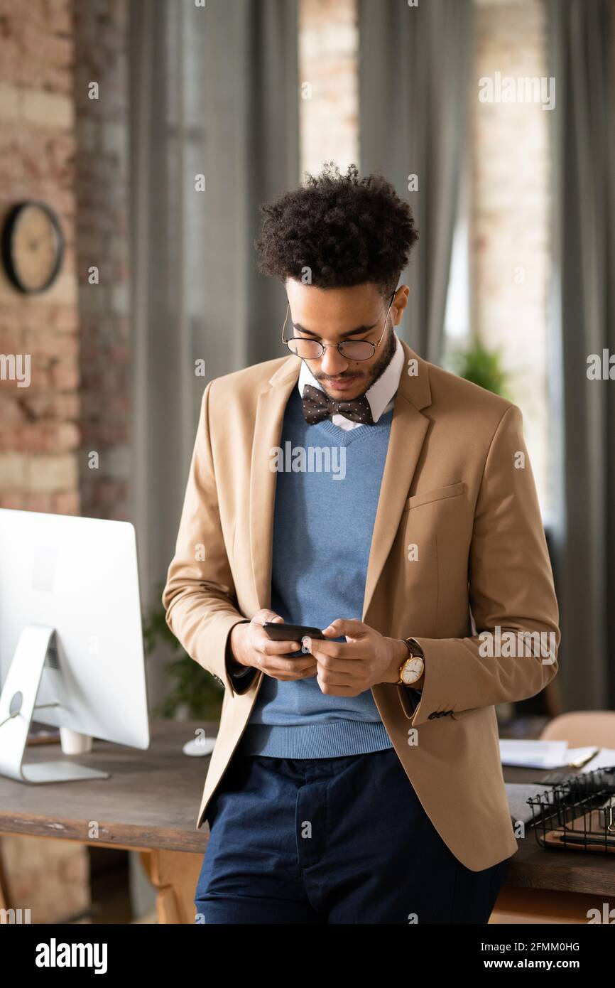 Jeune Noir concentré dans noeud papillon debout au bureau tableau et vérification des messages téléphoniques Banque D'Images