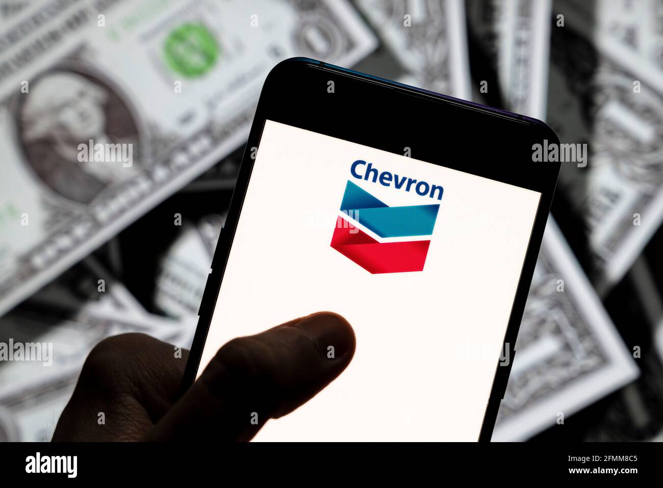 Sur cette photo, le logo de la multinationale américaine Chevron Corporation, qui est affiché sur un smartphone, est en arrière-plan avec une devise américaine (dollar américain). Banque D'Images