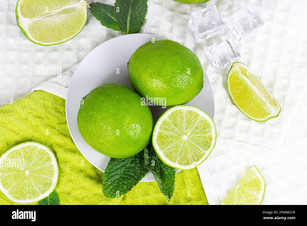 Vue de dessus des limes vertes fraîches juteuses et des tranches de citron vert avec feuilles de menthe dans la cuisine sur fond clair. Banque D'Images