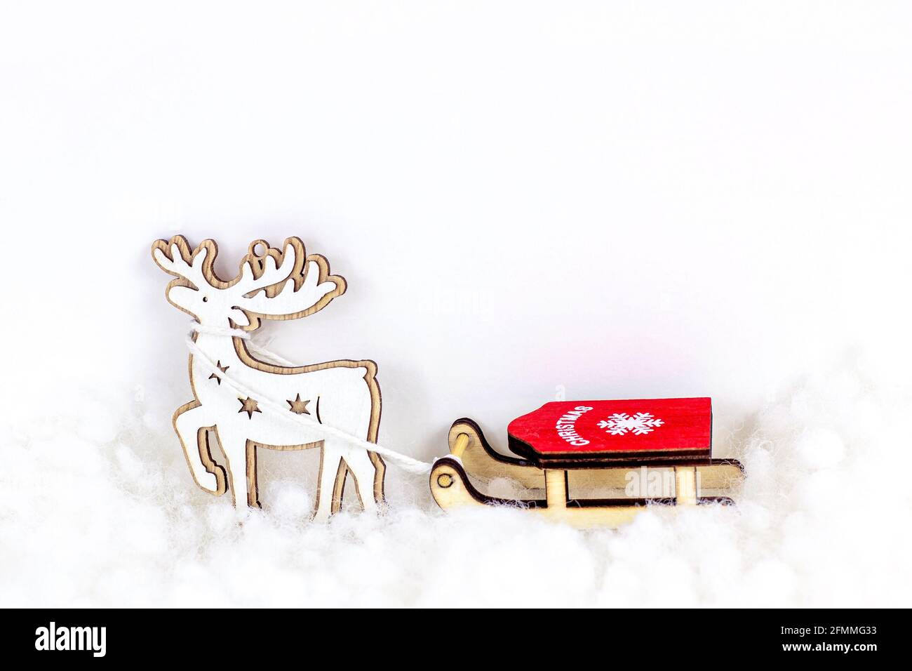 Renne en bois avec traîneau rouge sur fond de neige artificielle blanche avec espace pour les copies. Concept de célébration des fêtes de Noël et du nouvel an. Banque D'Images