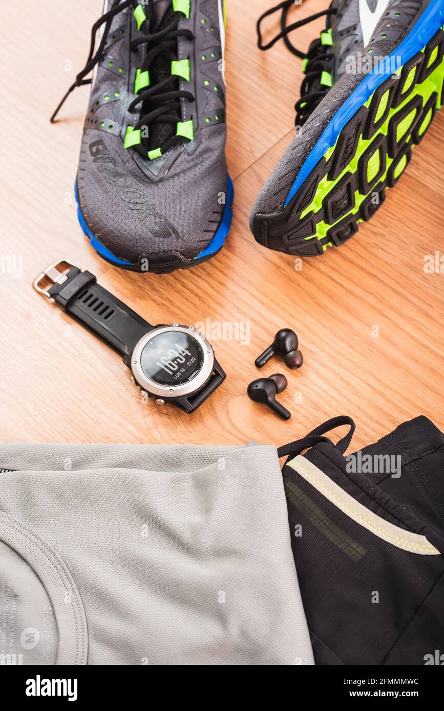 Valence, Espagne - 9 mai 2021 : chaussures de course à pied Brooks et montre de sport Garmin, grandes marques d'équipements sportifs, sur le sol avant une course d'athlétisme. Banque D'Images