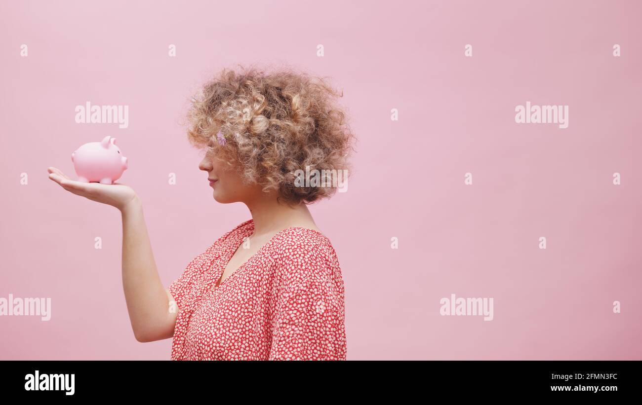 Femme tenant une petite banque de porc dans sa main et faisant des visages drôles. Grande attente faible croissance des investissements. Photo de haute qualité Banque D'Images