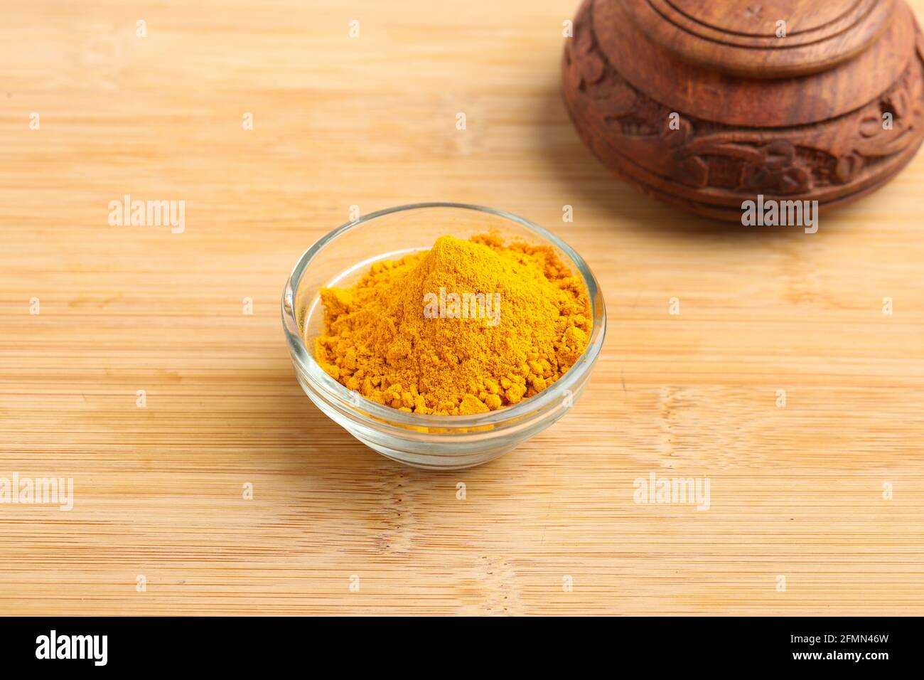 Poudre de curcuma dans un bol en verre sur fond de bois. Banque D'Images