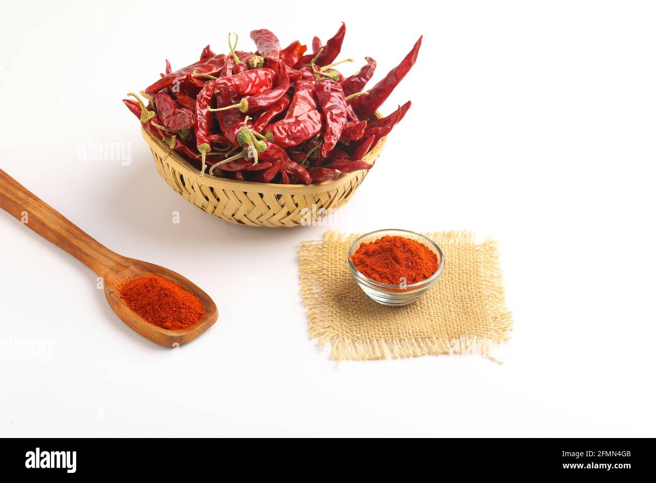 Piment rouge séché et poudre de piment rouge dans un bol en verre et cuillère en bois sur fond blanc Banque D'Images