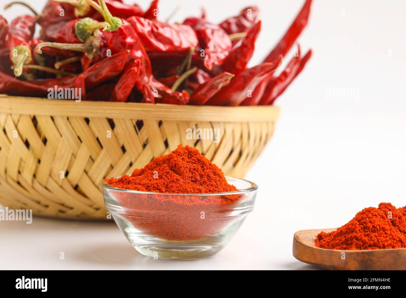 Piment rouge séché et poudre de piment rouge dans un bol en verre et cuillère en bois sur fond blanc Banque D'Images