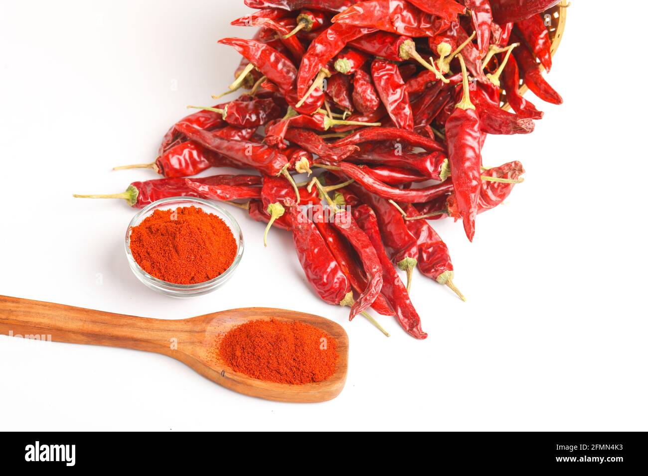 Piment rouge séché et poudre de piment rouge dans un bol en verre et cuillère en bois sur fond blanc Banque D'Images