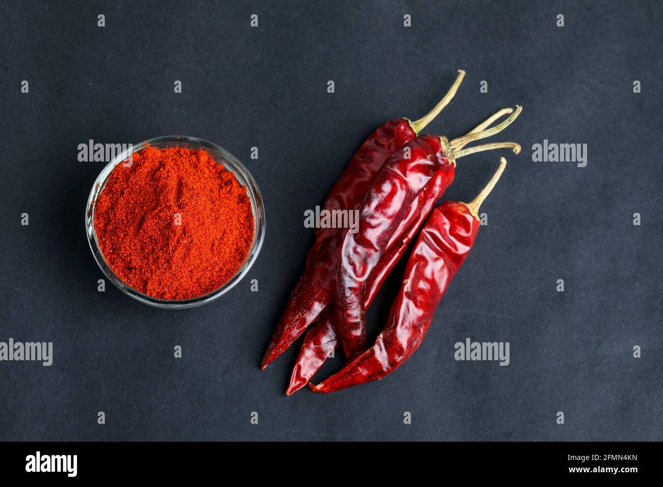 Piment rouge séché et poudre dans un bol en verre sur fond sombre. Banque D'Images