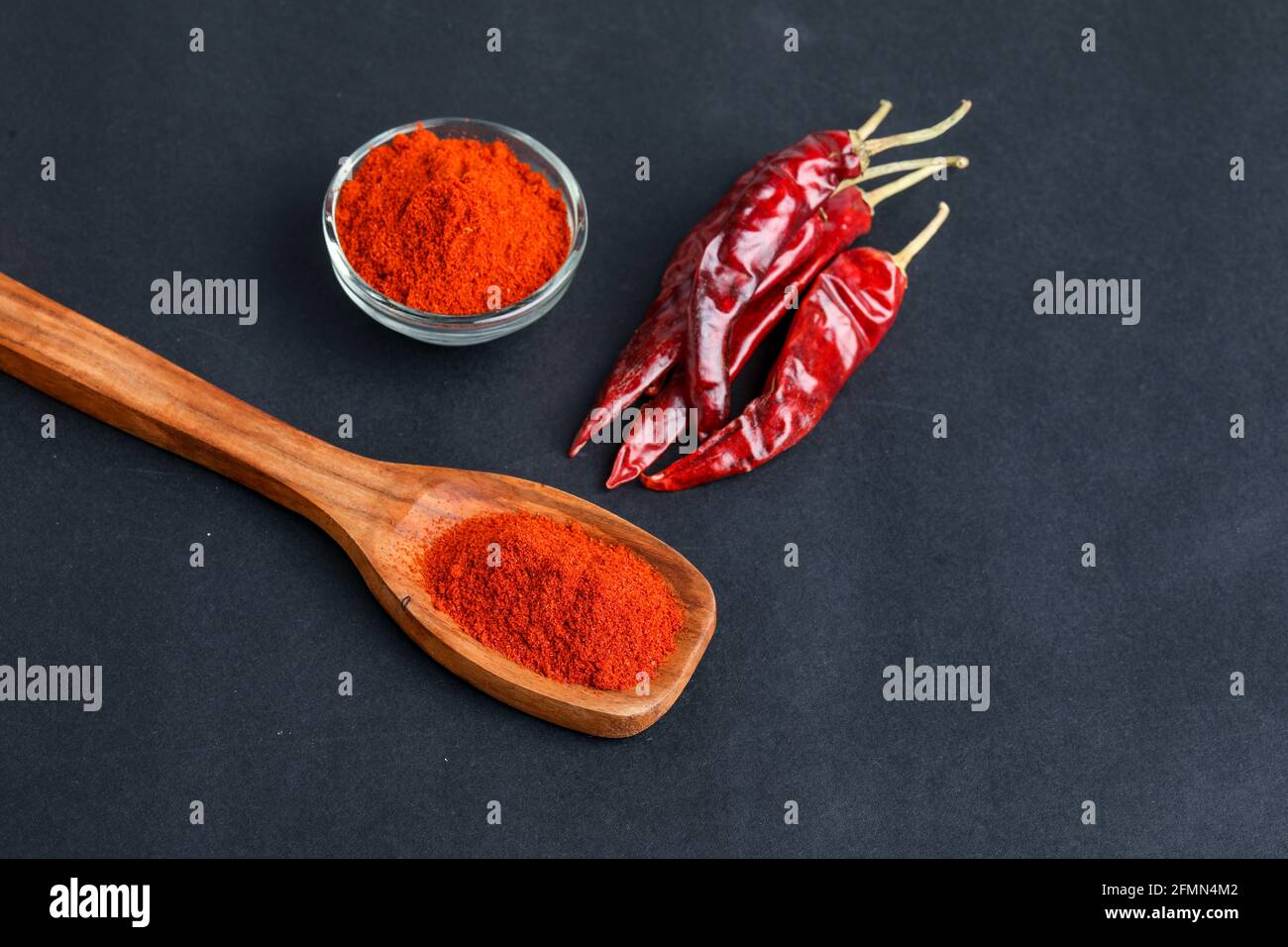 Piment rouge séché et poudre dans un bol en verre et une cuillère en bois sur fond sombre. Banque D'Images