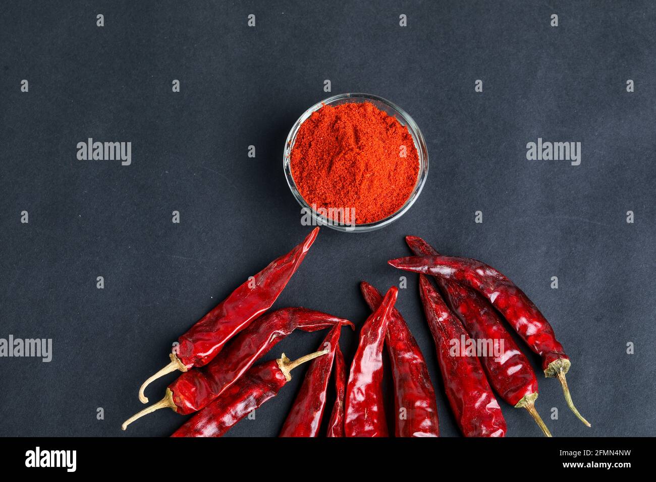 Piment rouge séché et poudre dans un bol en verre sur fond sombre. Banque D'Images