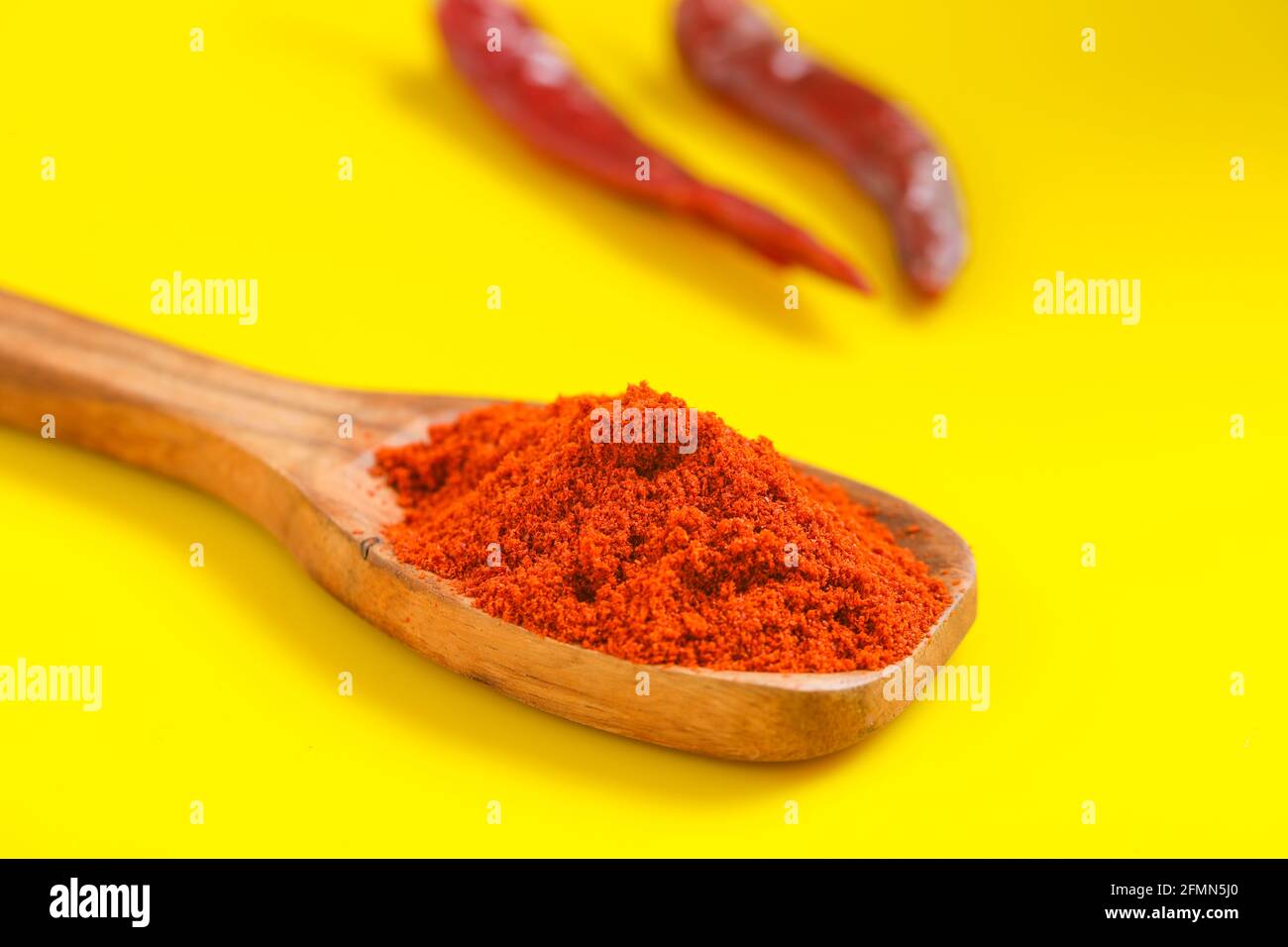 Poudre de Chili dans une cuillère en bois avec un froid rouge sec sur fond jaune. Banque D'Images