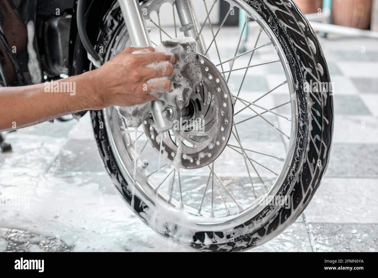 Gros plan de la main d'un homme lavant les roues d'une moto avec des éponges et des bulles. Banque D'Images Gros plan de la main d'un homme lavant les roues d'une moto avec des éponges et des bulles. Banque D'Images