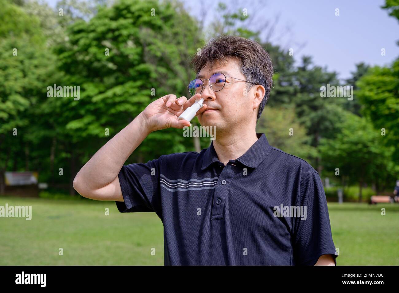 Homme asiatique d'âge moyen utilisant un spray nasal à l'extérieur. Banque D'Images