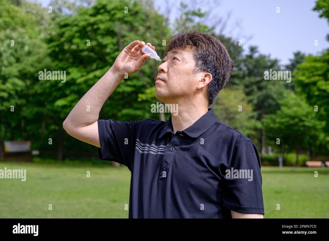 Homme asiatique d'âge moyen mettant des gouttes d'oeil dans ses yeux à l'extérieur. Banque D'Images