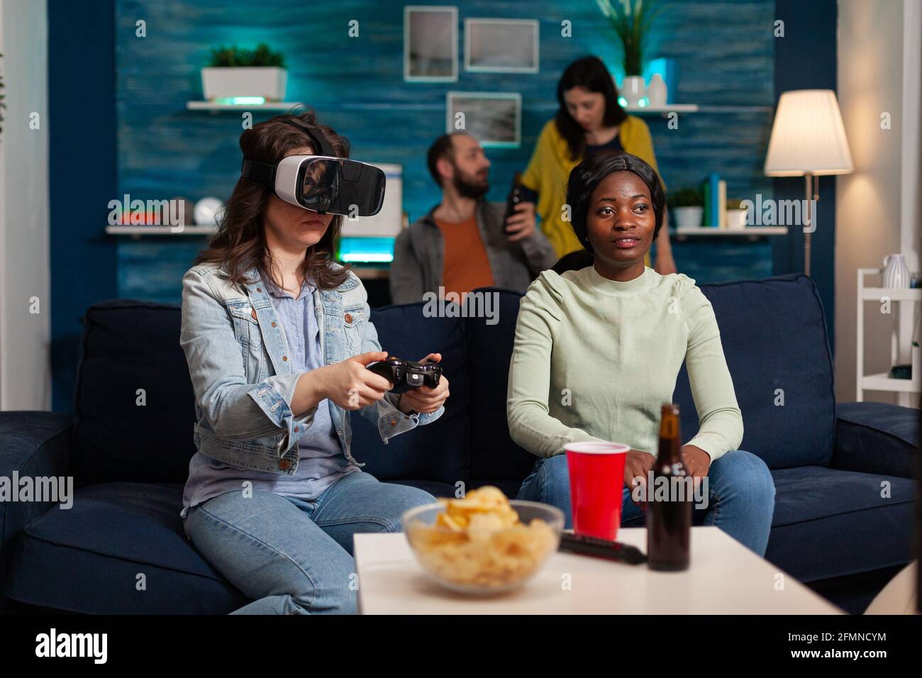 Une femme excitée qui passe du temps avec des amis de course mixtes et qui vit des jeux de réalité virtuelle avec un casque vr pendant la compétition. Groupe multiethnique qui s'amuse ensemble. Banque D'Images