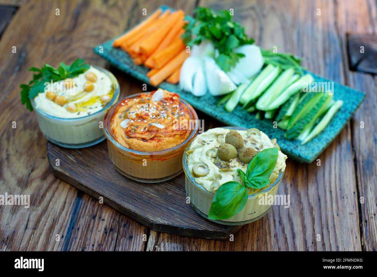 houmous classiques avec paprika et ail, olives, pois chiches, tahini, huile d'olive, et des épices orientales dans un bol sur une table en bois avec des légumes frais Banque D'Images
