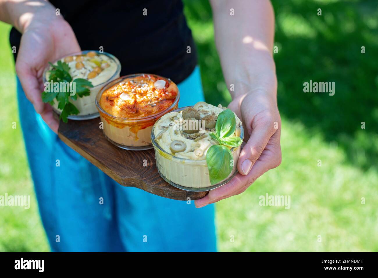 Trois types d'appétissants hummus classiques avec paprika et ail, olives, pois chiches, tahini, huile d'olive et épices orientales dans les mains des femmes. Traditionnel Banque D'Images