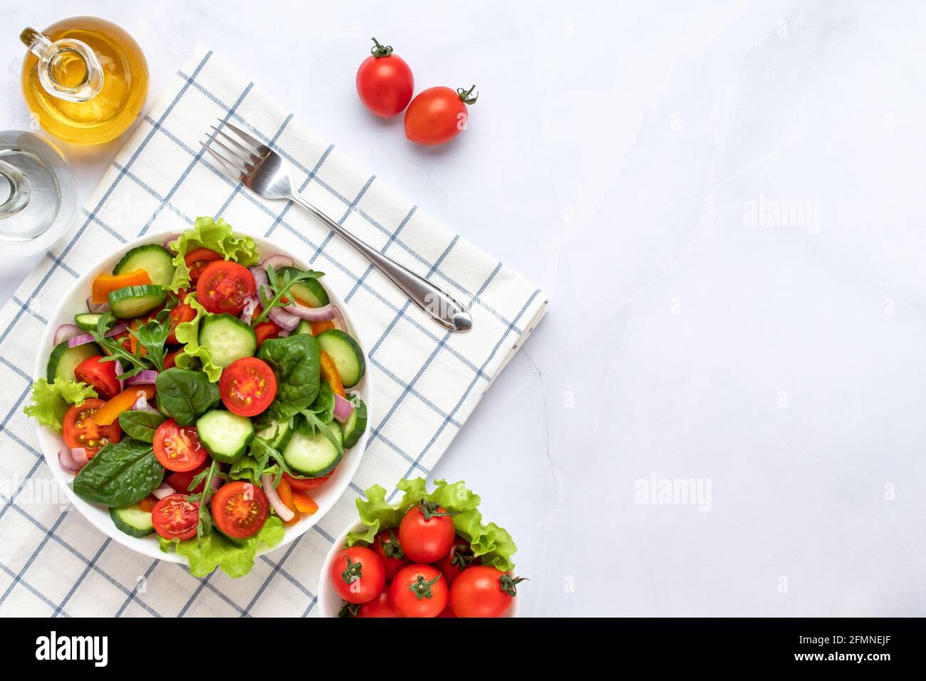 Légumes sur une plaque blanche sur fond de marbre gris. Vue de dessus. Salade faite de tomates cerises, concombres, arugula, basilic et garnie d'olive Banque D'Images
