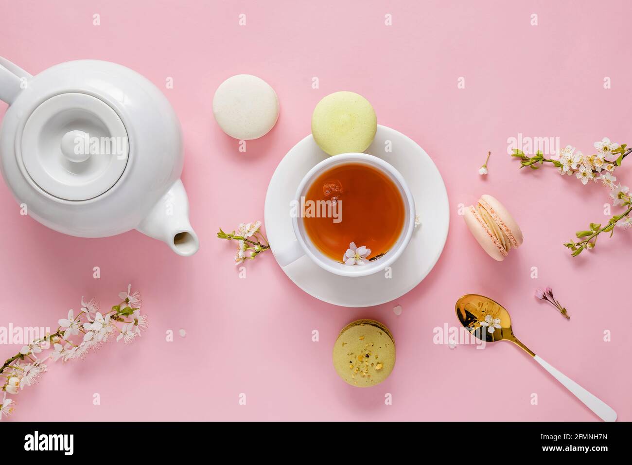 Macarons, thé et fleurs sur fond rose. Banque D'Images