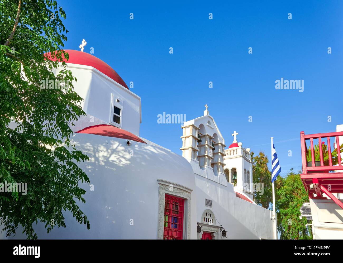 Église orthodoxe grecque traditionnelle dans la ville grecque de l'île. Dôme rouge, murs blanchis à la chaux, drapeau grec et clocher. Mykonos, Cyclades, Grèce. Banque D'Images