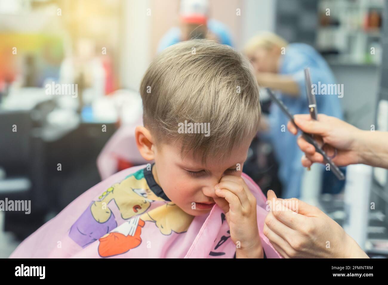 Coupe De Cheveux Garcon Blond Petit garçon blond avec une couverture colorée enlève les cheveux du nez  après une coupe de cheveux avec un styliste qualifié dans un salon de  beauté moderne de près Photo Stock -
