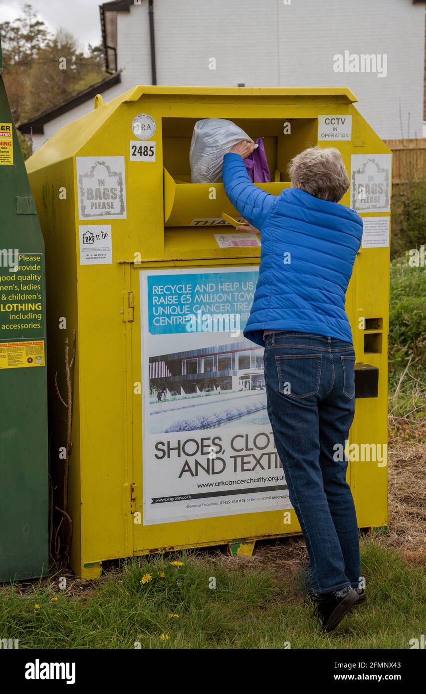 Hampshire, Angleterre, Royaume-Uni. 2021. Femme faisant don de vêtements pour une œuvre de charité en utilisant un conteneur de collecte communautaire pour la charité dans un village du Hampshire. Banque D'Images