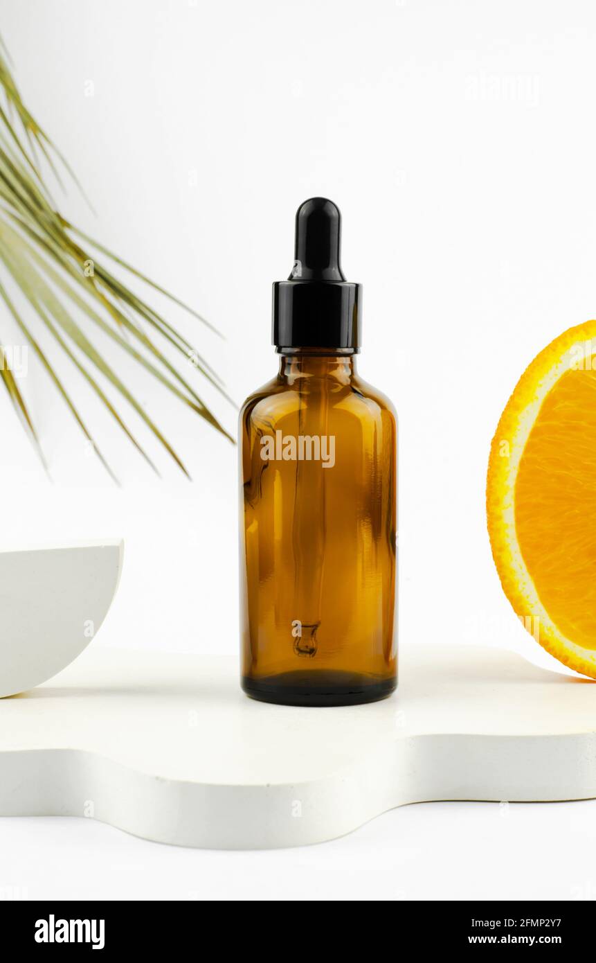 Sérum dans un flacon en verre avec une pipette. Huile essentielle naturelle sur un podium blanc. Emballage d'un produit cosmétique. Huiles à l'extrait d'orange Banque D'Images