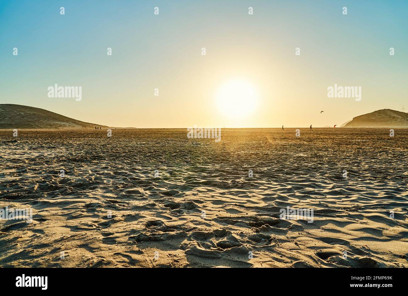 Sable de la plage de Prasonisi contre les hautes collines et les personnes marchant Au coucher du soleil à l'horizon le jour de fin d'été en Grèce Banque D'Images